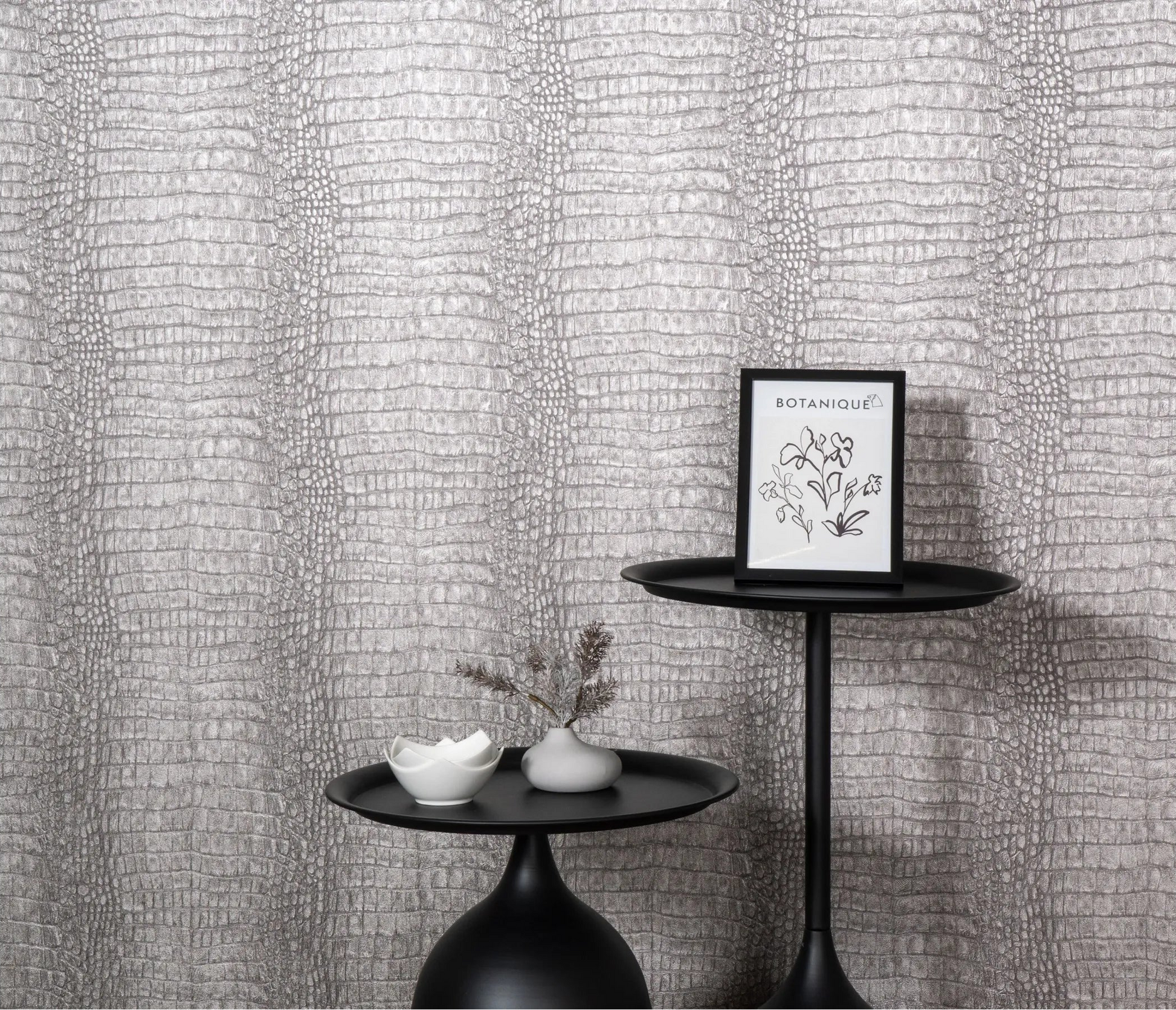 Erismann Forest Dreams 10560-37 wallpaper on a grey reptile-skin textured wall behind black pedestal tables and framed botanical print.