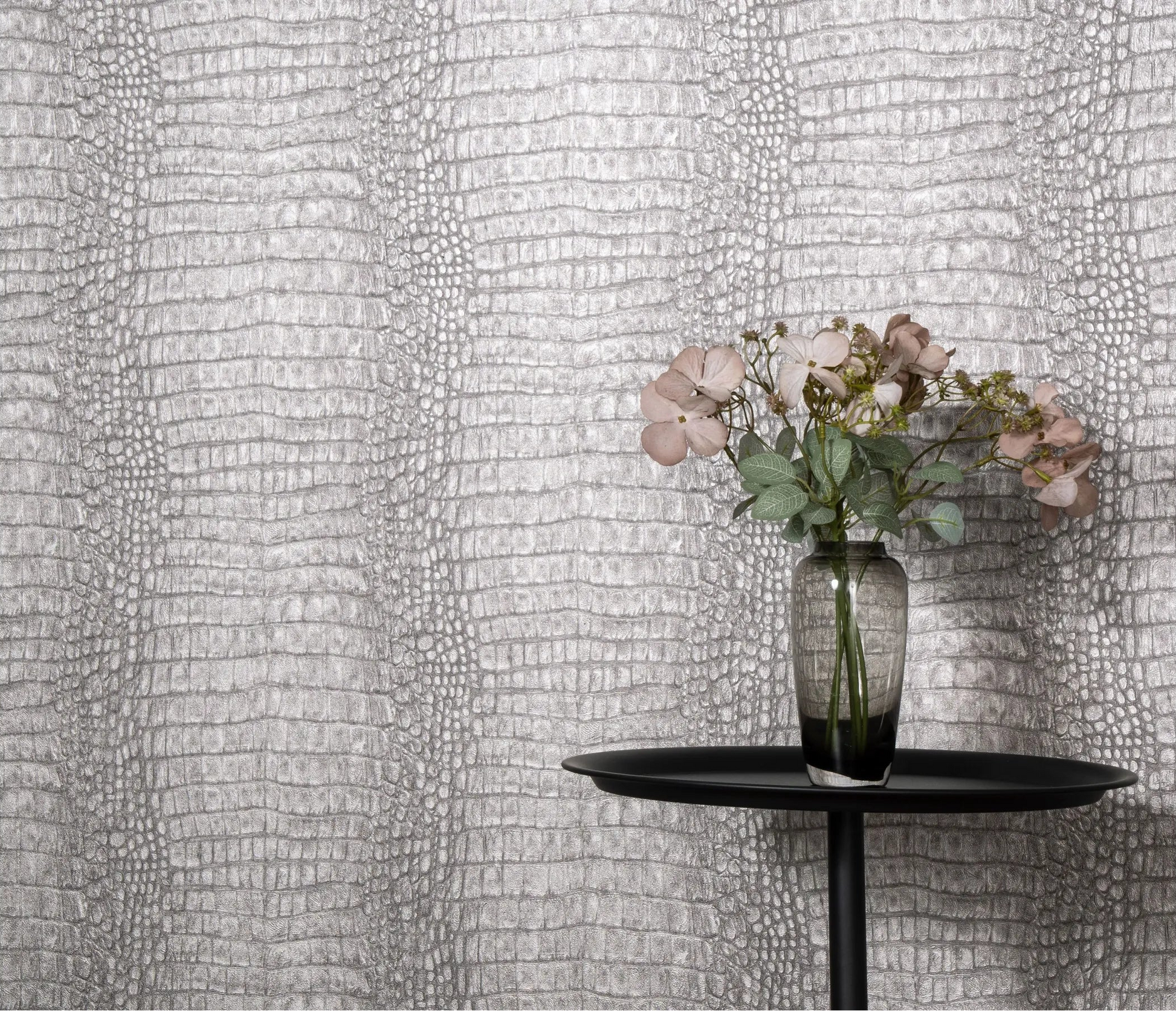 Erismann Forest Dreams 10560-37 wallpaper on a textured grey reptile-skin patterned wall behind a black round table and flower vase.