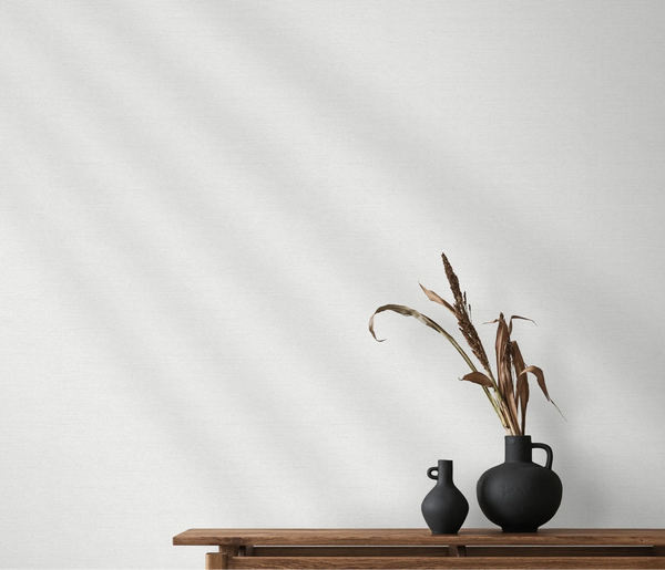 Erismann Forest Dreams 10563-01 wallpaper on a pale textured wall behind a wooden console with black vases and dried stems.