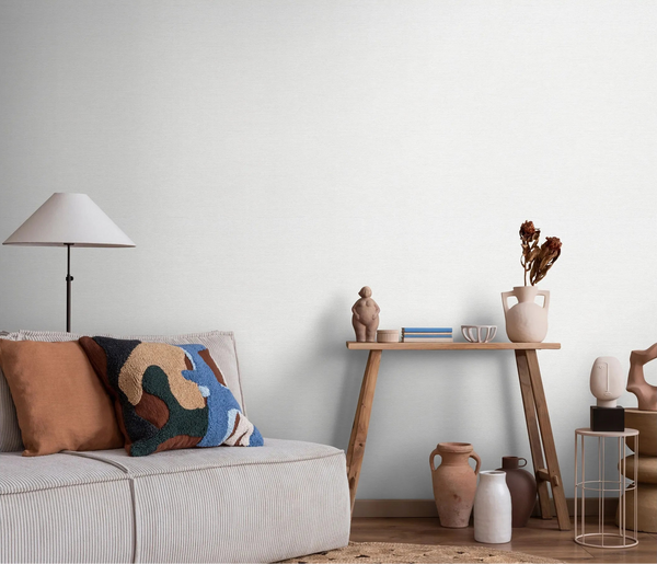 Erismann Forest Dreams 10563-01 wallpaper on a pale textured living room wall behind a sofa, floor lamp, and wooden console table.