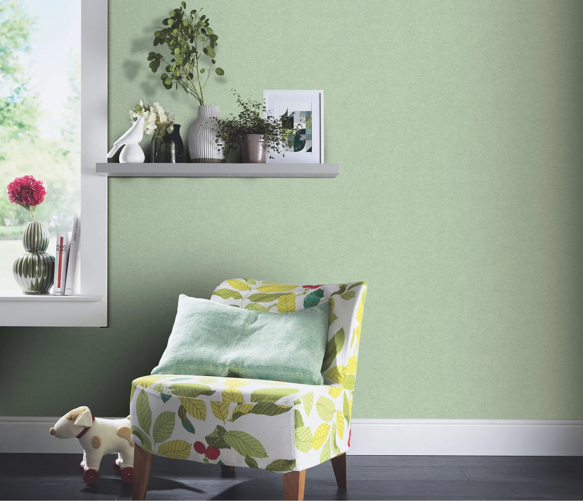 Erismann Forest Dreams 10563-07 wallpaper on a green textured wall behind a leaf-patterned chair, shelf decor, and window.