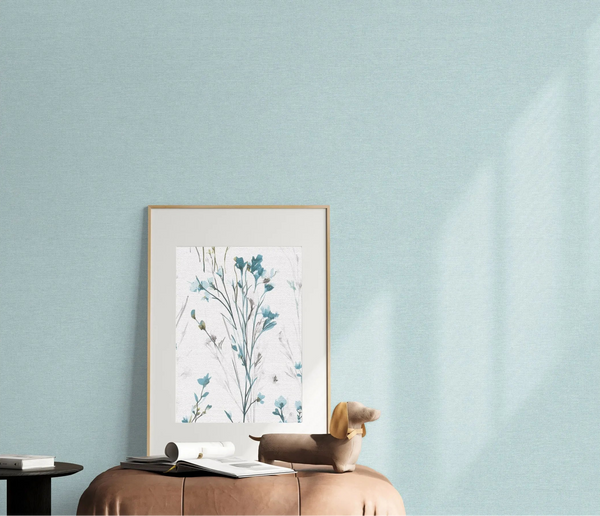 Erismann Forest Dreams 10563-43 wallpaper on a pale blue textured wall behind framed botanical art and a leather ottoman.