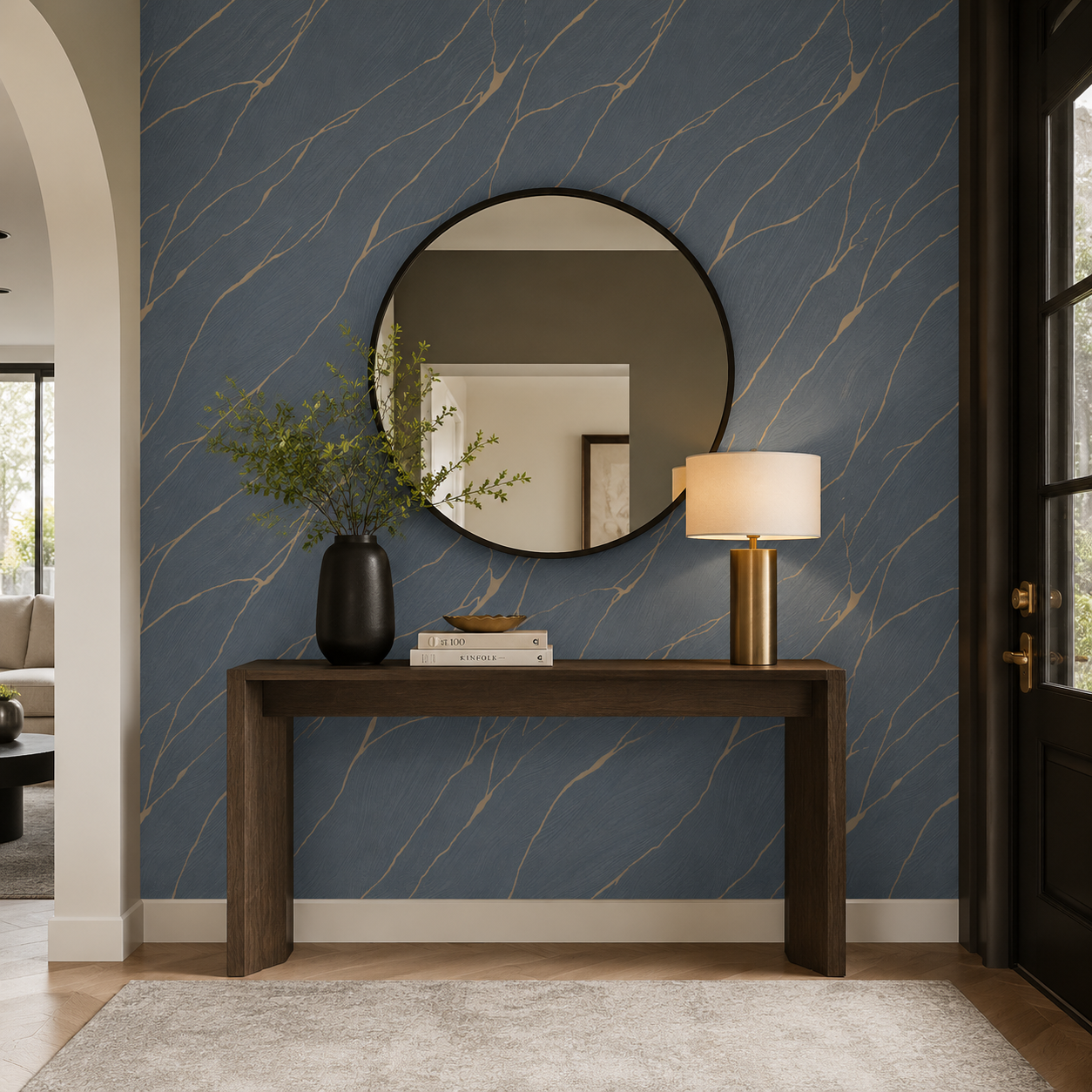 Erismann Opus 10440-08 blue and gold marble-effect wallpaper in a modern entryway with a round black mirror, wood console table, brass lamp, black vase, and warm contemporary styling.