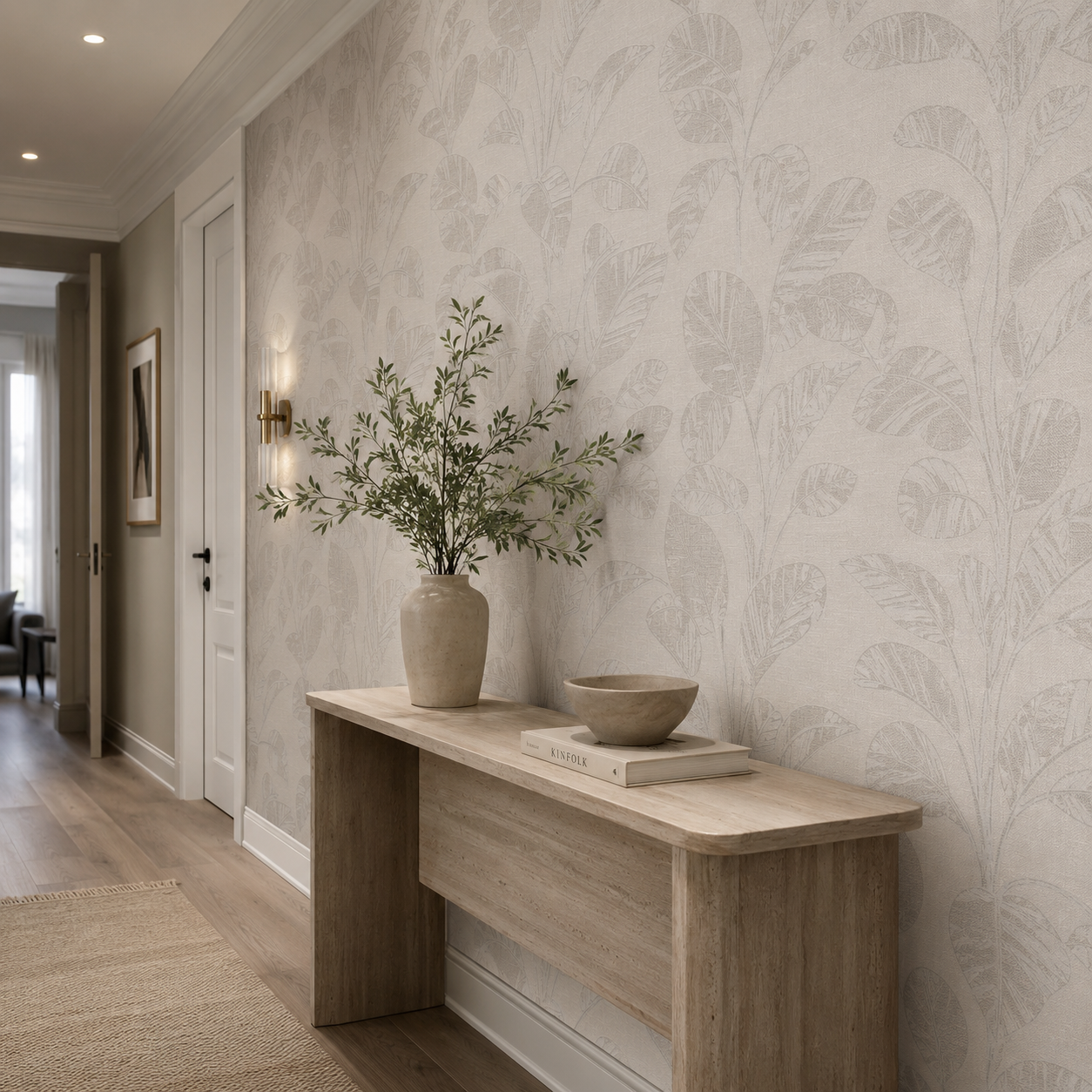 Erismann Opus 10459-02 light neutral botanical leaf wallpaper in an elegant hallway with a natural wood console table, ceramic vase, soft wall lighting, and refined neutral interior styling.