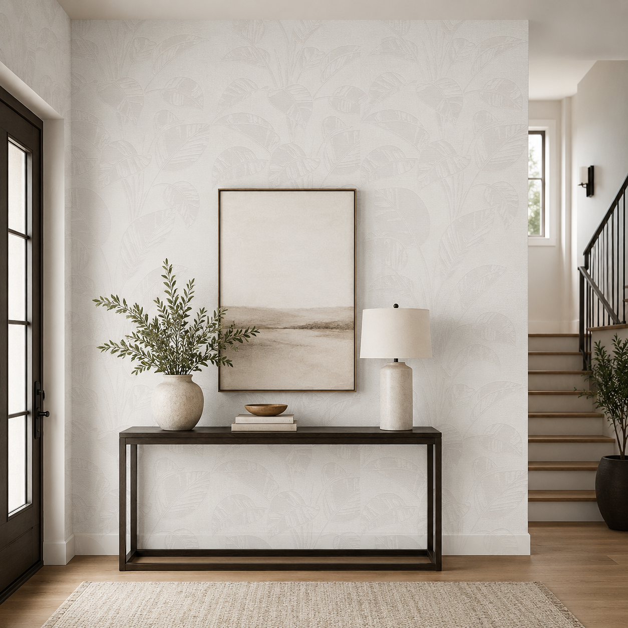 Erismann Opus 10459-14 warm neutral botanical leaf wallpaper in a bright entryway with a slim console table, framed artwork, ceramic lamp, greenery, staircase, and soft modern styling.
