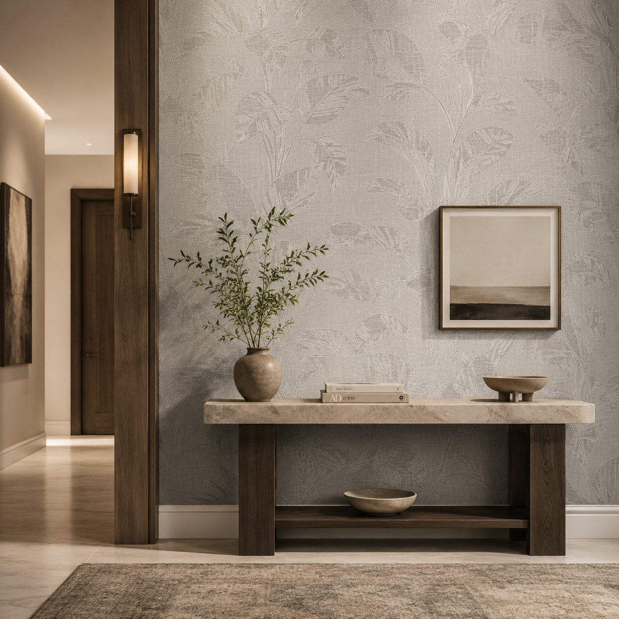 Erismann Opus 10459-24 soft grey botanical leaf wallpaper in an elegant hallway with a stone console table, natural wood legs, ceramic vase, framed artwork, and warm contemporary lighting.