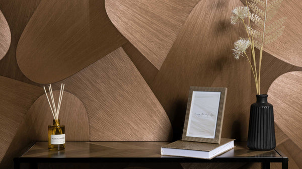 Erismann Elysium abstract geometric wallpaper with layered curved shapes in rich bronze and deep brown tones, installed in a modern interior setting, creating a warm and sophisticated backdrop that enhances decorative accents and textured surfaces.