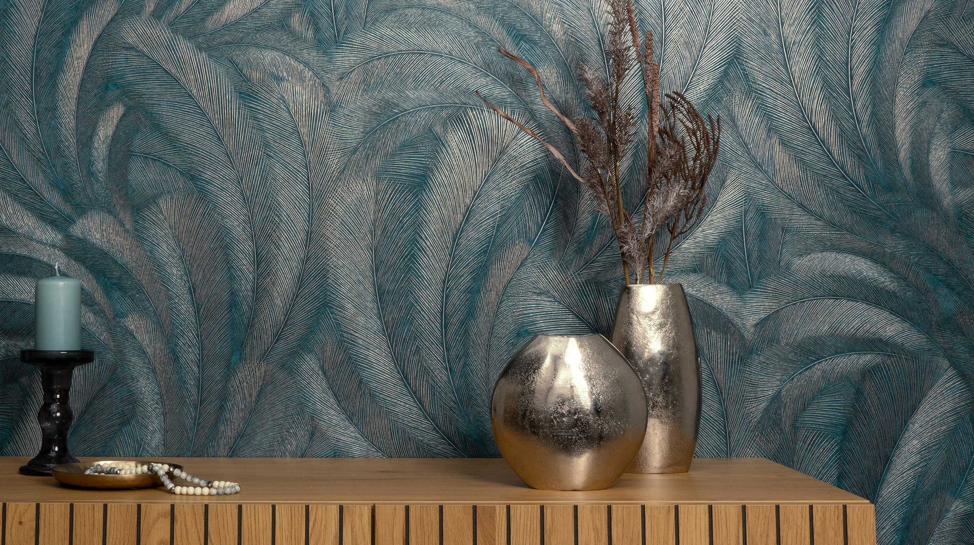 Erismann Elysium botanical feather wallpaper in rich teal and metallic tones, installed as a feature wall behind a console table, creating a dramatic and elegant backdrop that enhances warm wood textures and decorative accents in a modern interior.
