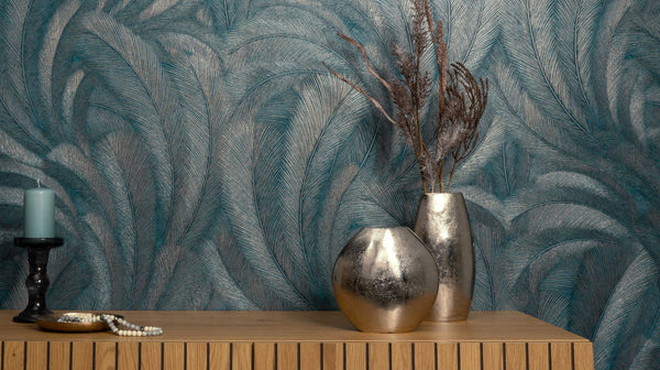 Erismann Elysium botanical feather wallpaper in rich teal and metallic tones, installed as a feature wall behind a console table, creating a dramatic and elegant backdrop that enhances warm wood textures and decorative accents in a modern interior.