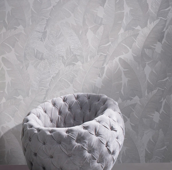 Marburg Avalon 31623 Tonal grey wallpaper with large overlapping leaf motif behind a round tufted chair on a plain floor.