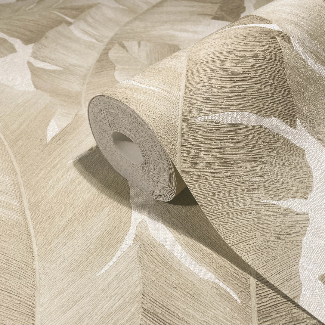Marburg Avalon 31625 Close-up of a beige wallpaper roll with a large leaf pattern resting on the matching unrolled wallpaper.