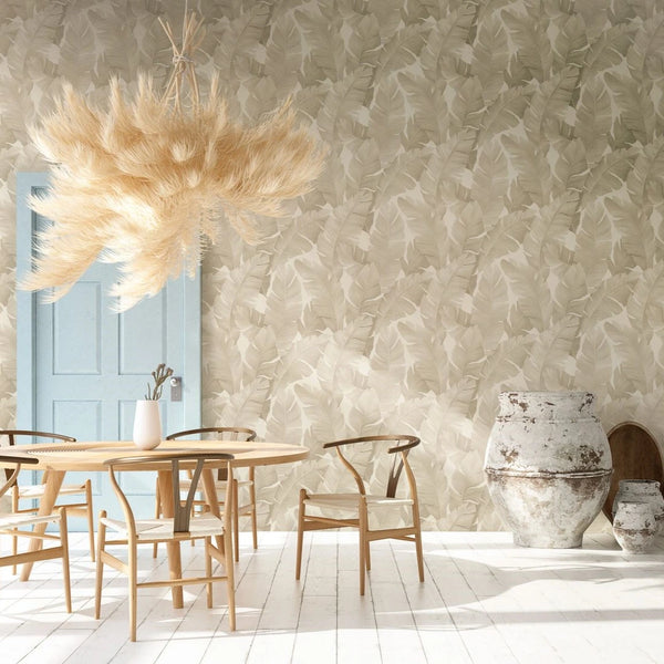 Marburg Avalon 31625 Dining room scene featuring beige leaf-pattern wallpaper, a light blue door, a round wooden table with chairs, a feathery pendant light, and large rustic ceramic pots on a white painted floor.