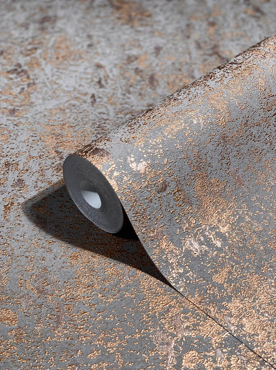 Marburg Avalon 31644 Close-up of a wallpaper roll with a raised copper metallic mottled pattern on a gray background, partially unrolled on the same wallpaper.