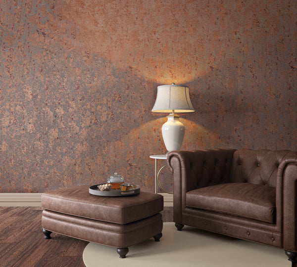 Marburg Avalon 31644 Mottled copper and gray textured-effect wallpaper behind a brown leather armchair, a matching ottoman with a tea tray, and a white table lamp.