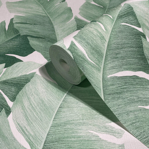 Marburg Avalon 31650 Close-up of a wallpaper roll featuring large green tropical leaves on a white background, shown resting on the same pattern.