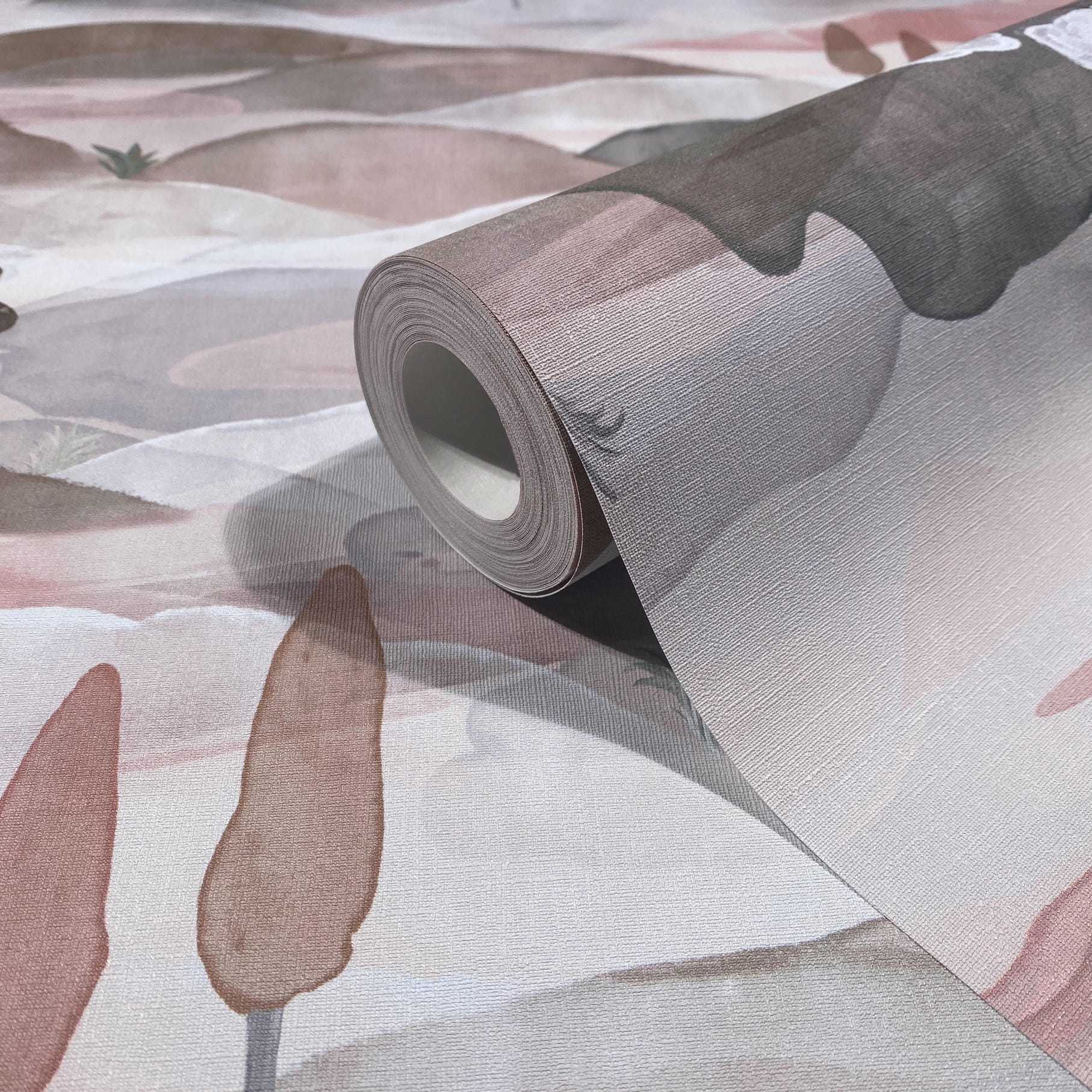 Marburg Boho 35786 Wallpaper roll resting on matching textured paper with a soft, painterly abstract pattern in pink, taupe, and gray hues.