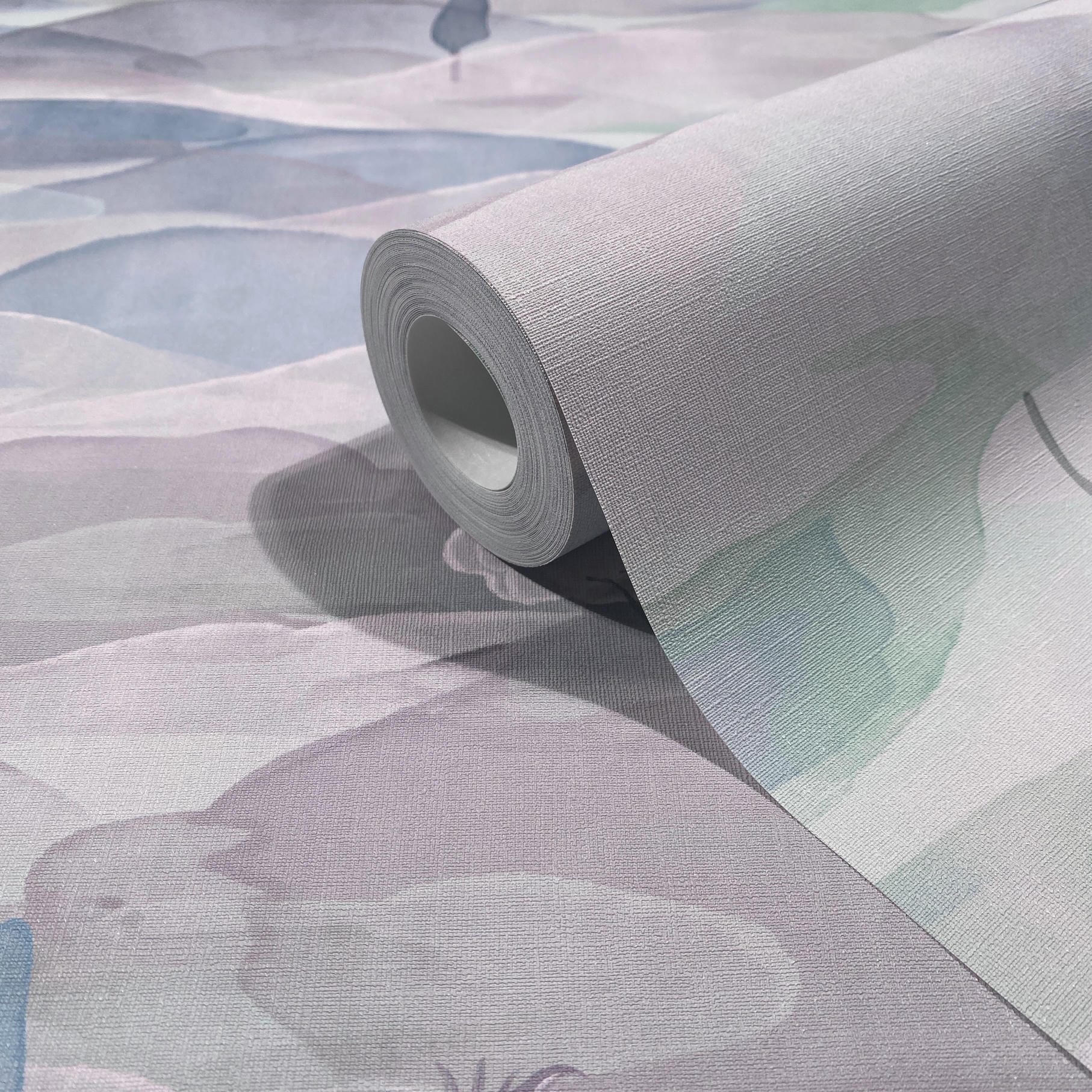 Marburg Boho 35788 Close-up of a textured wallpaper roll resting on matching unrolled sheet, showing abstract watercolor-style shapes in soft blue and green on a light ground.