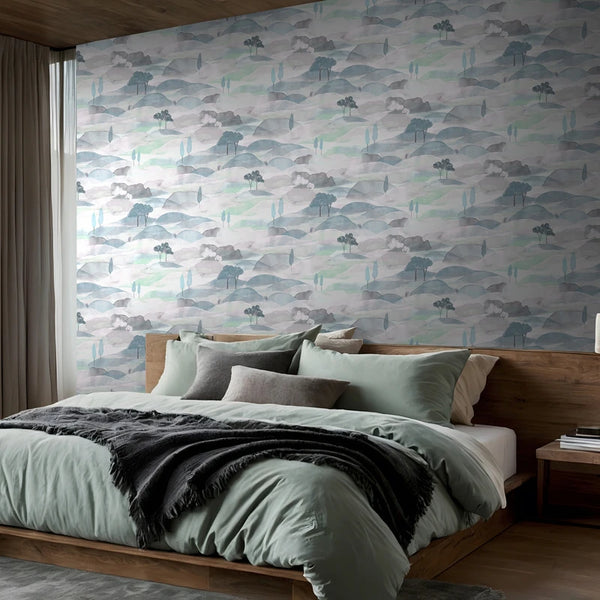 Marburg Boho 35788 Watercolor landscape wallpaper with layered hills and small trees in soft blue, green, and gray on the wall behind a bed in a modern bedroom.