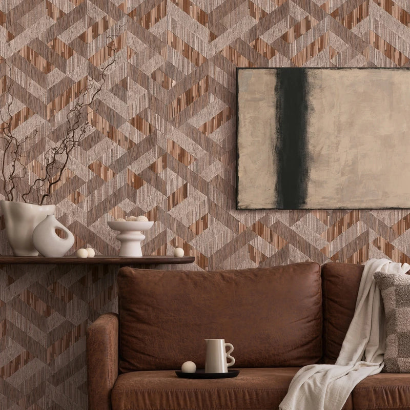 Marburg Boho 35789 Geometric brown and taupe wallpaper with interlocking angled bands and fine vertical striations, shown behind a brown leather sofa with a pillow and throw, a floating shelf with white ceramic vases and branches, small decorative spheres, a mug on a tray, and a.