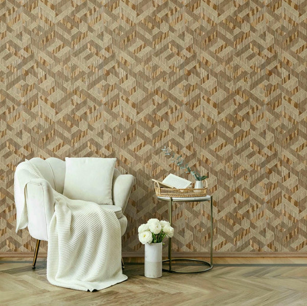 Marburg Boho 35790 Beige and brown geometric wallpaper with a 3D cube effect shown in a room setting with a white armchair, a round side table holding a tray with a book and small vase, and a floor vase with white flowers on a herringbone wood floor.