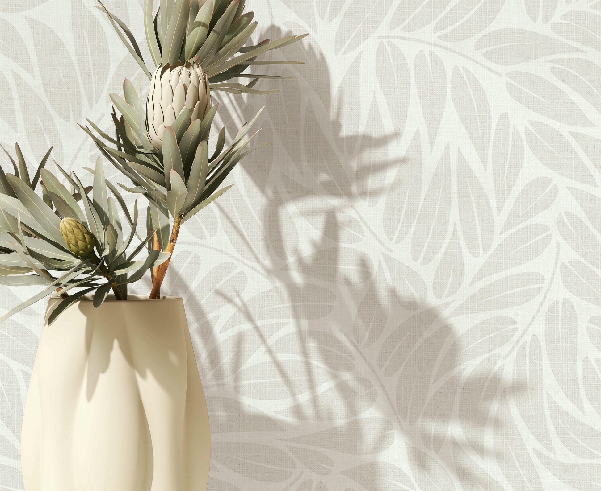 Marburg Boho 35794 Close-up of light grey and white leaf-pattern wallpaper with a cream vase holding botanical stems at the left, casting soft shadows on the wall.