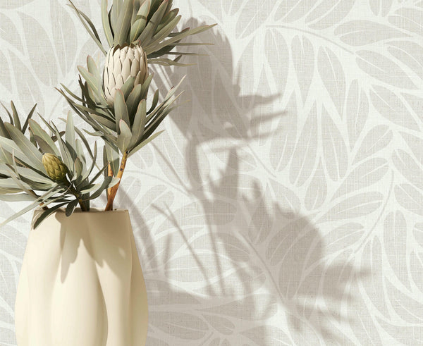 Marburg Boho 35794 Close-up of light grey and white leaf-pattern wallpaper with a cream vase holding botanical stems at the left, casting soft shadows on the wall.