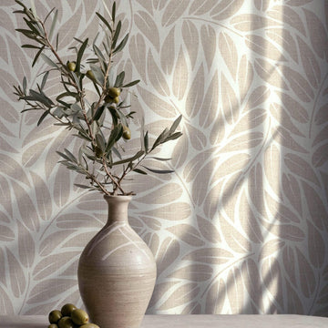 Marburg Boho 35795 Beige leaf-pattern wallpaper with a subtle woven texture, styled with a ceramic vase holding an olive branch and a few olives on a tabletop.