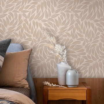 Marburg Boho 35796 Beige wallpaper with a large overlapping leaf pattern behind a bed and a wooden bedside table holding two vases with dried stems.