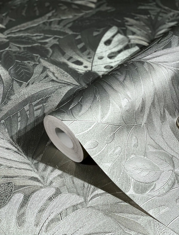 Marburg Botanica 33302 Close-up of a wallpaper roll showing an embossed tropical leaf pattern with a metallic sheen, resting on the same patterned surface.