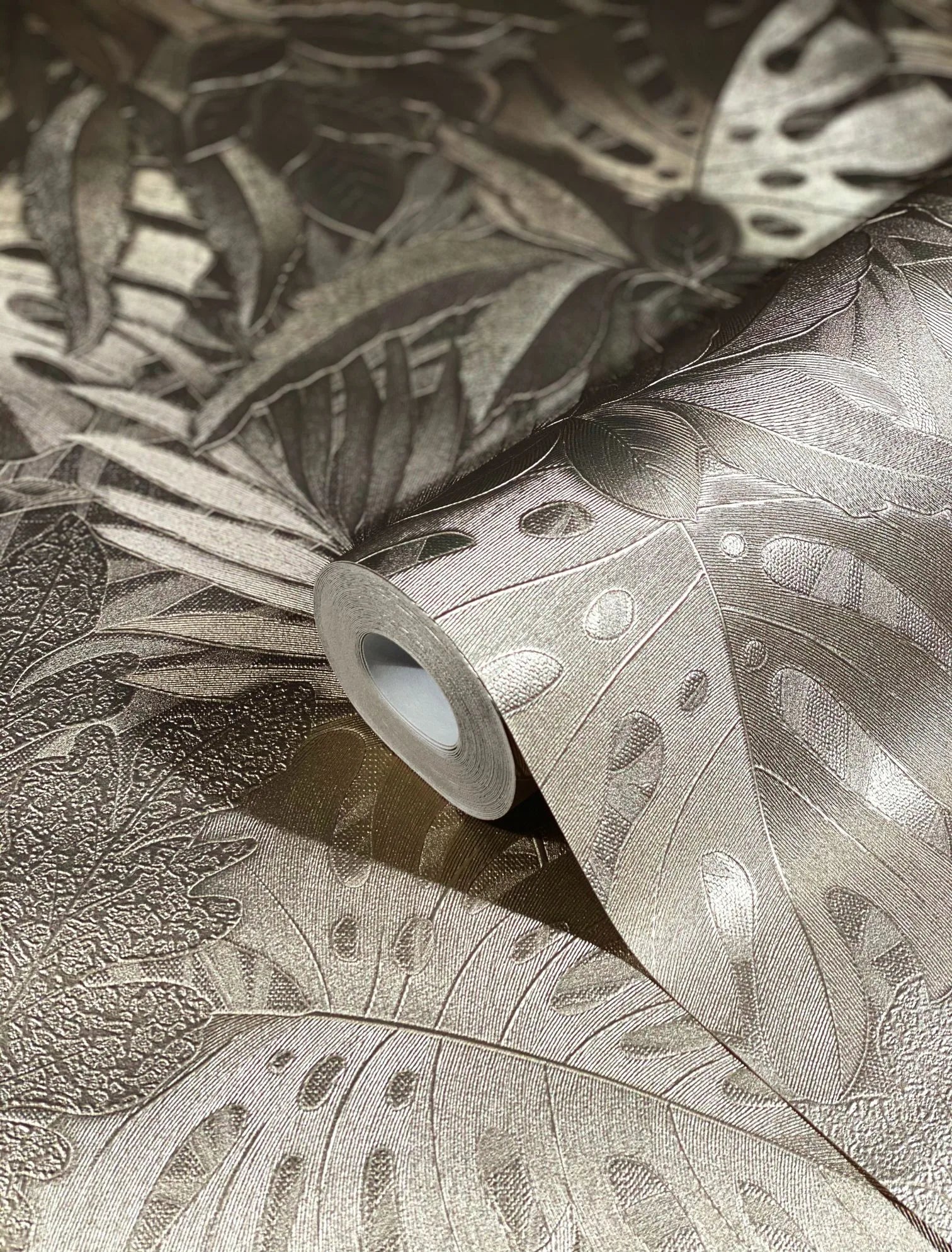 Marburg Botanica 33303 Close-up of a wallpaper roll on matching unrolled paper showing an embossed metallic gold tropical leaf pattern with large monstera leaves.