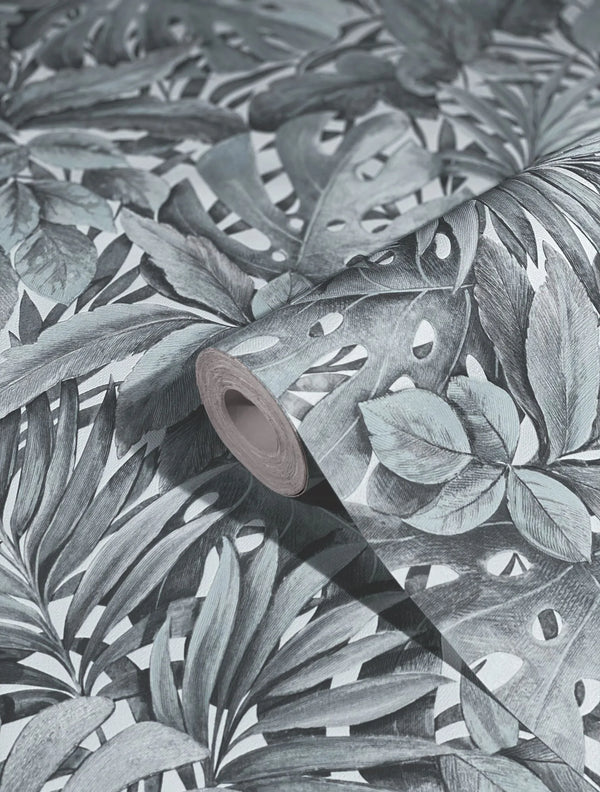 Marburg Botanica 33306 Close-up of a wallpaper roll resting on matching paper with a dense tropical leaf pattern, showing layered palm and split-leaf foliage in muted green tones on a light background.