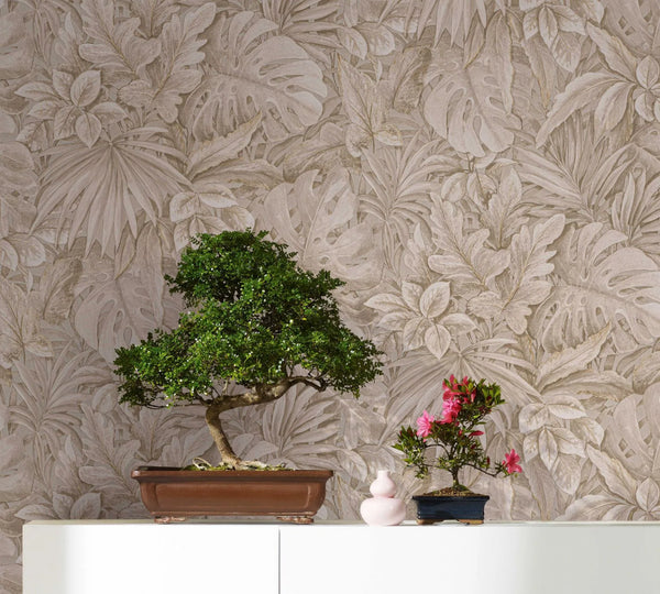 Marburg Botanica 33307 Beige botanical leaf wallpaper forms the backdrop for a scene with a bonsai tree, a smaller flowering bonsai, and a small pink vase on a white cabinet.