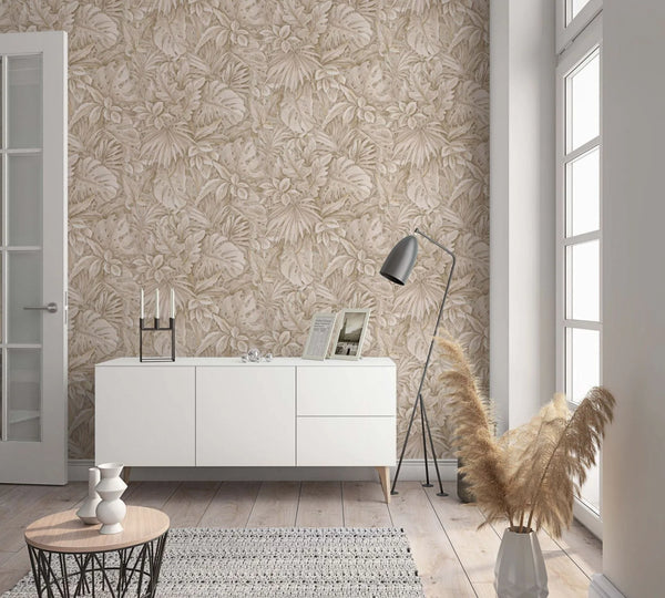 Marburg Botanica 33307 Room scene with beige tropical leaf wallpaper behind a white sideboard, a black floor lamp, a round coffee table, and pampas grass in a vase by a large window.