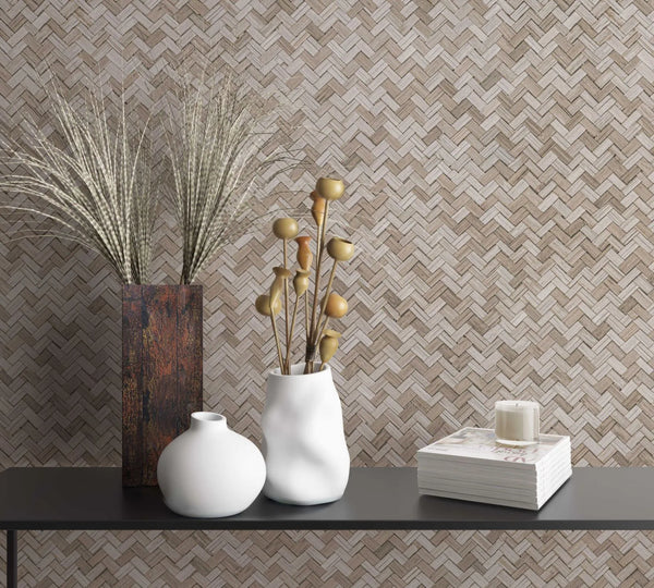 Marburg Botanica 33309 Beige and taupe herringbone wallpaper behind a black console holding a tall rectangular vase with dried grasses, two white vases with dried stems, a stack of books, and a small candle.