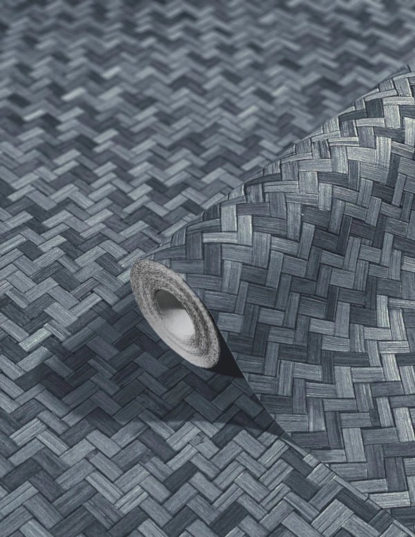 Marburg Botanica 33310 Angled wallpaper roll resting on matching unrolled wallpaper, showing a dark charcoal woven herringbone basketweave pattern.