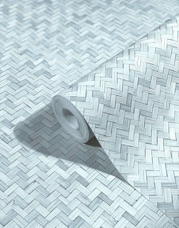 Marburg Botanica 33312 Angled wallpaper roll on a matching surface showing an interlaced herringbone weave pattern in light blue‑gray tones.