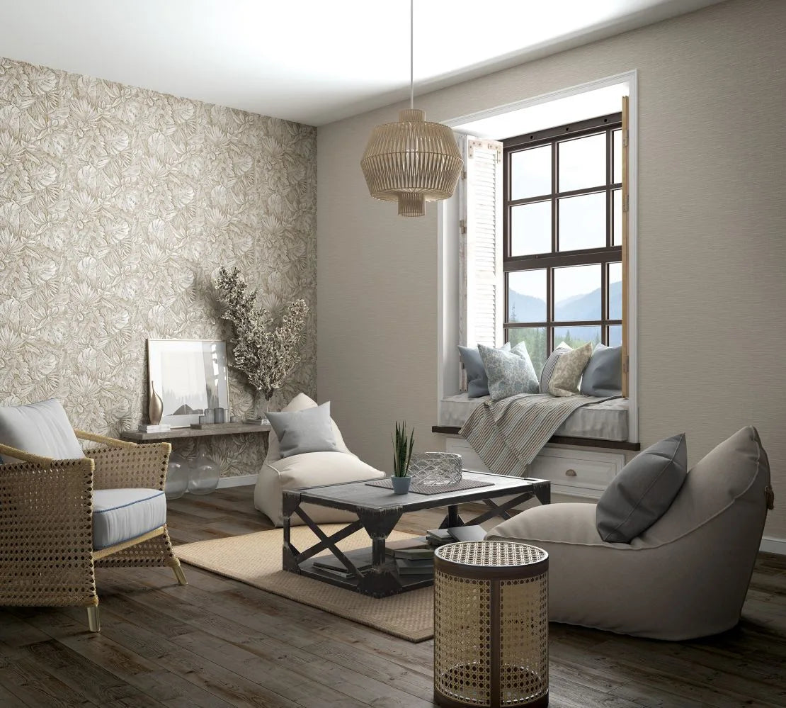 Marburg Botanica 33316 Living room scene with a beige botanical wallpaper feature wall, a window seat with cushions, rattan pendant, cane armchair, coffee table, side table, and rug on wooden floors.