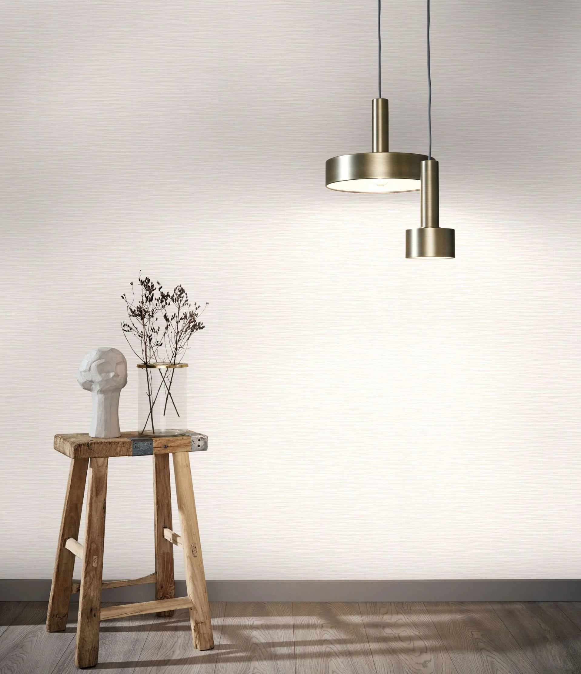Marburg Botanica 33318 Light beige and white wallpaper with a fine horizontal texture shown on a feature wall, styled with a wooden stool holding a sculpted head and a glass vase with dried stems beneath two metal pendant lights; wood floor and baseboard visible.