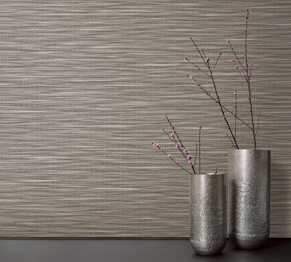 Marburg Botanica 33319 Textured brown wallpaper with horizontal striations, styled with two tall silver vases holding branches with small pink blossoms on a dark surface.