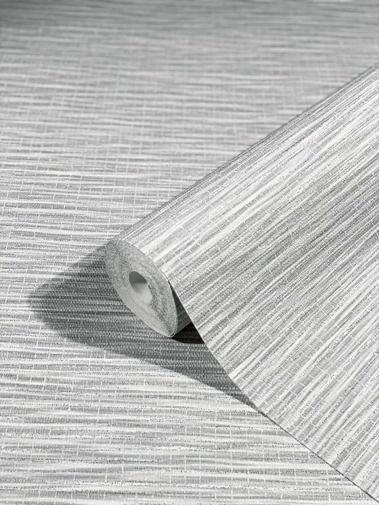 Marburg Botanica 33323 A gray textured wallpaper roll with fine horizontal striations resting on the same patterned sheet.