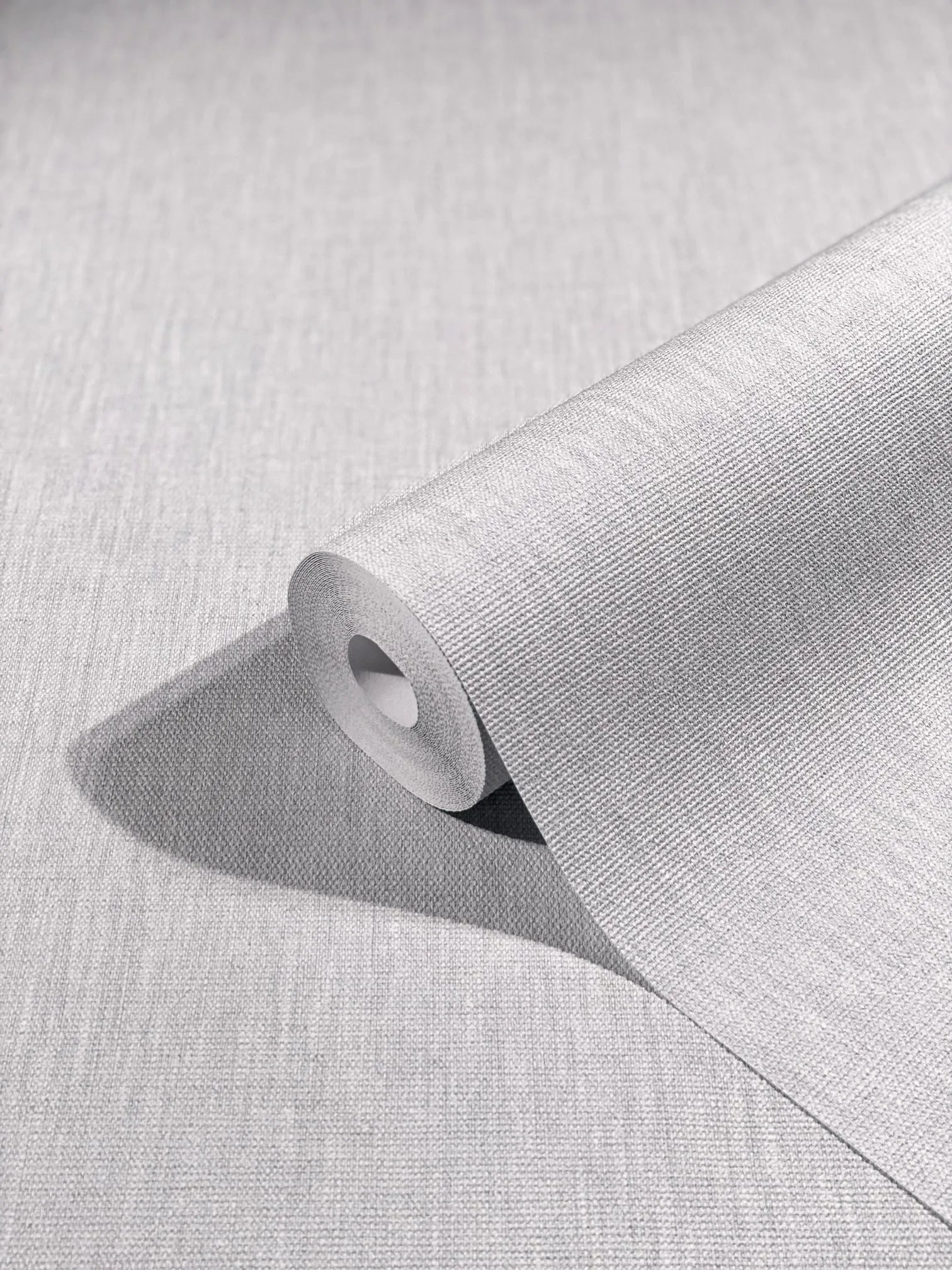 Marburg Botanica 33324 A light gray textured wallpaper roll partially unrolled on a matching surface, showing a fine woven linen-like pattern.