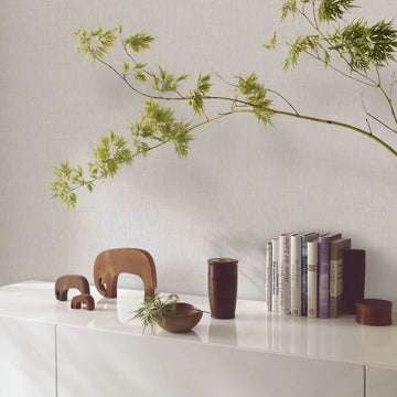 Marburg Botanica 33324 Light beige-gray textured wallpaper behind a white sideboard styled with wooden elephant figurines, a wooden bowl and cup, books, and a leafy branch.