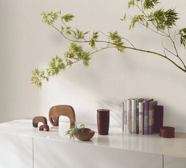 Marburg Botanica 33325 Light gray textured wallpaper with a fine linen look behind a white cabinet styled with wooden animal figures, books, a wooden bowl, and a leafy branch.