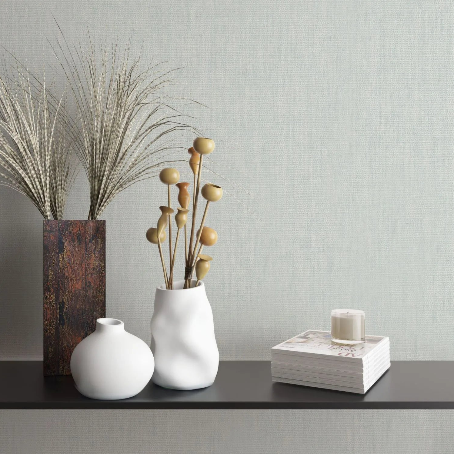 Marburg Botanica 33326 Light green textured wallpaper shown behind a black shelf styled with two white ceramic vases, dried stems, a tall rectangular vase with grasses, and a stack of books topped with a candle.