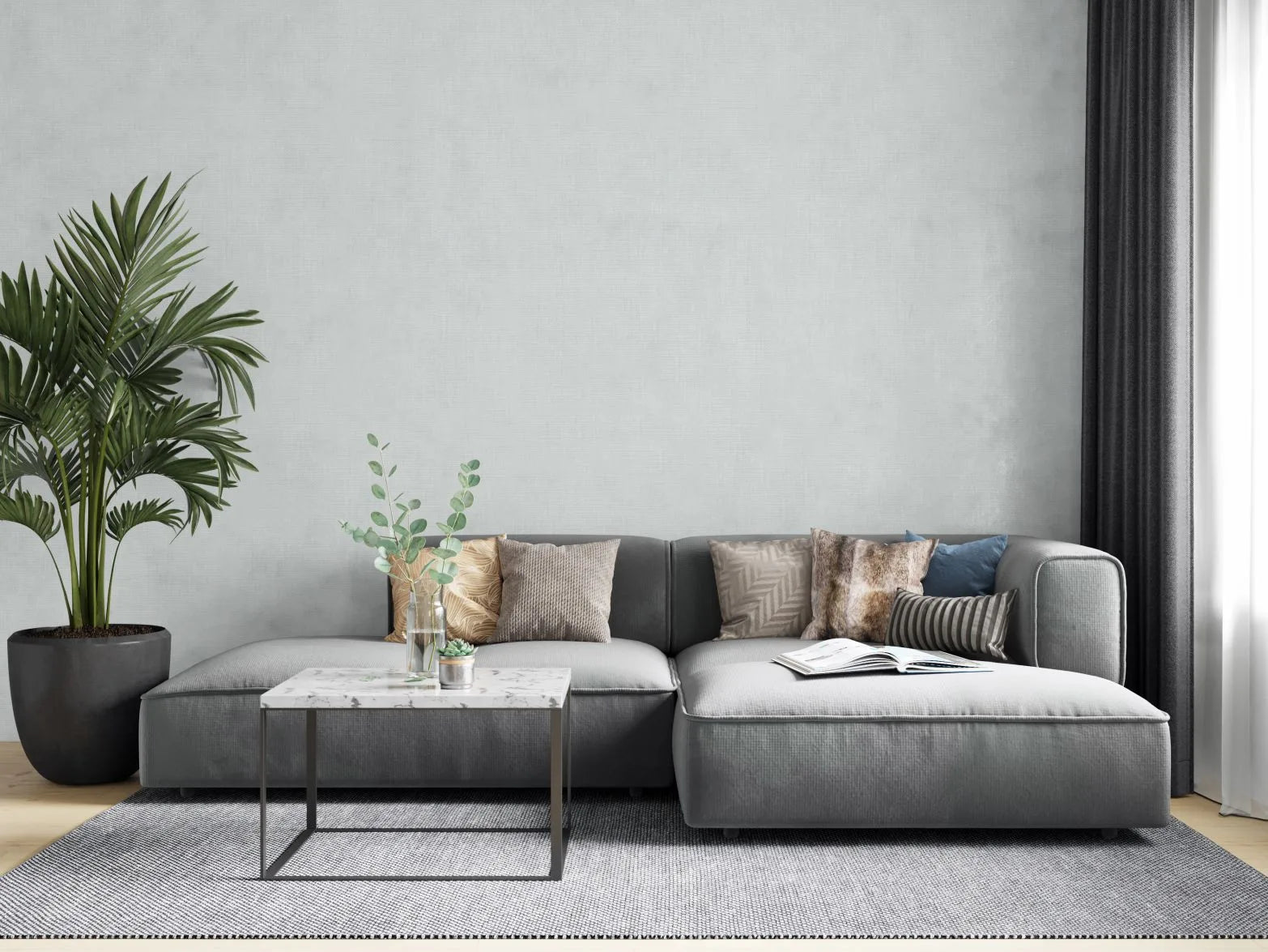 Marburg Botanica 33326 Living room scene showing a light gray textured wallpaper behind a gray sectional sofa with assorted cushions, a small marble-top coffee table with glass vases and a succulent, a large potted plant, a rug, and dark curtains by a window.