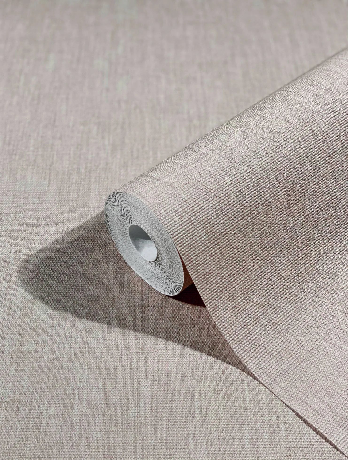Marburg Botanica 33327 Close-up of a beige textured wallpaper roll partially unrolled on a matching surface, showing a fine crosshatch pattern and cast shadow.