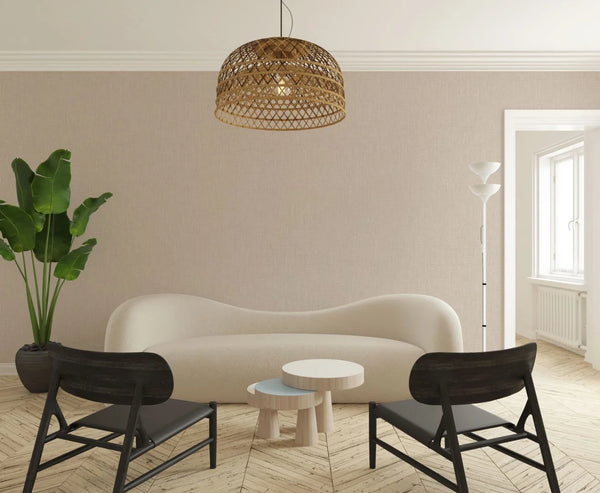 Marburg Botanica 33327 Living room scene showing beige textured wallpaper with a fine linen-look behind a curved cream sofa, two dark chairs, small round tables, a woven pendant light, a white floor lamp, a potted plant, and a window.