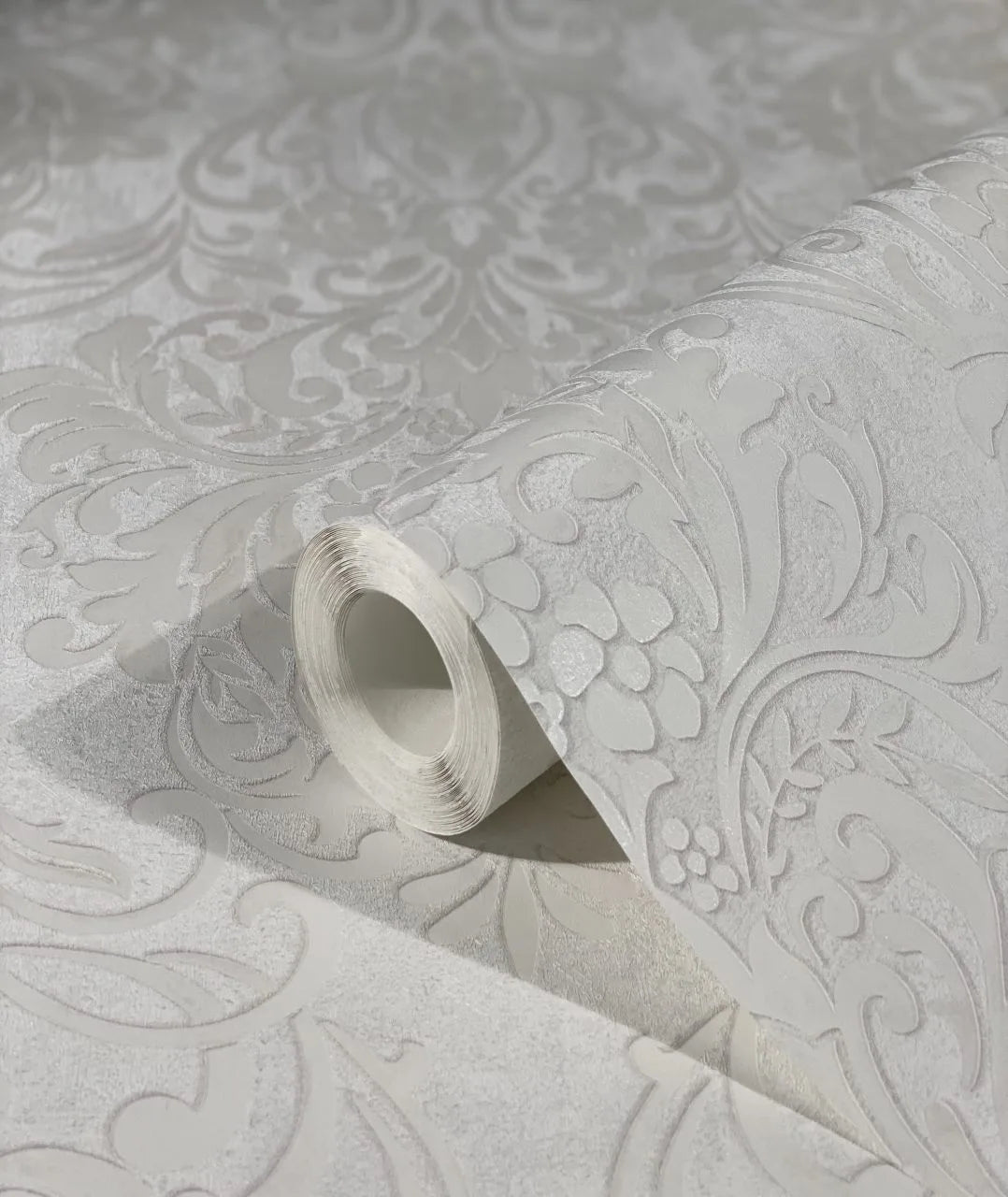 Marburg City Glam 32601 Wallpaper roll resting on an unrolled sheet showing a light gray raised damask pattern with a subtle sheen.