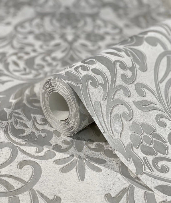 Marburg City Glam 32602 Close-up of a wallpaper roll with a gray damask scroll pattern resting on the same patterned surface.