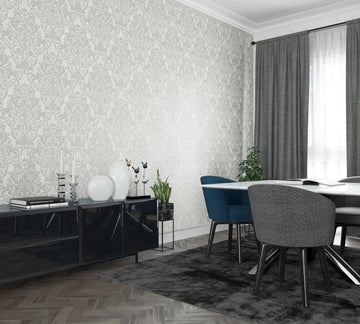 Marburg City Glam 32602 Room scene with a white wall covered in light gray damask wallpaper behind a dining table with blue and gray chairs, a black sideboard with decor, a window with gray curtains, a rug, and indoor plants.